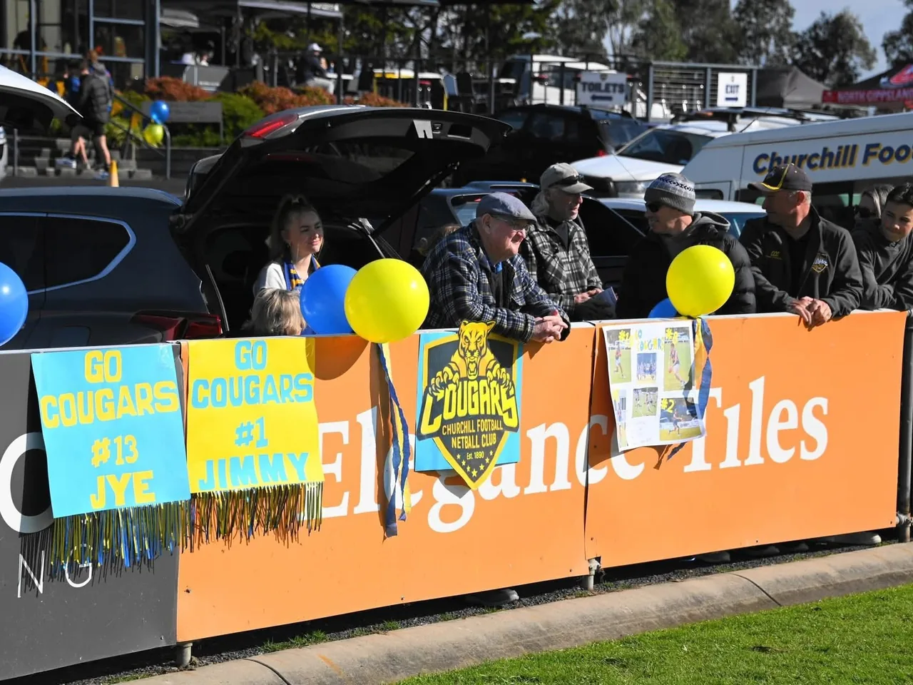 Cougars supporters on the fence at Gaskin Park on game day, with blue and gold balloons and Go Cougars signs